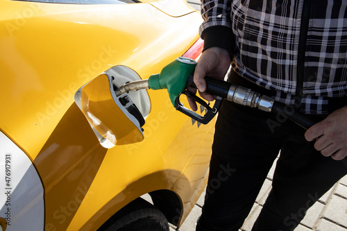 A man refueling a car at a gas station. The taxi driver pours fuel into the tank of the car. A man holds a refueling pistol in his hand. photo