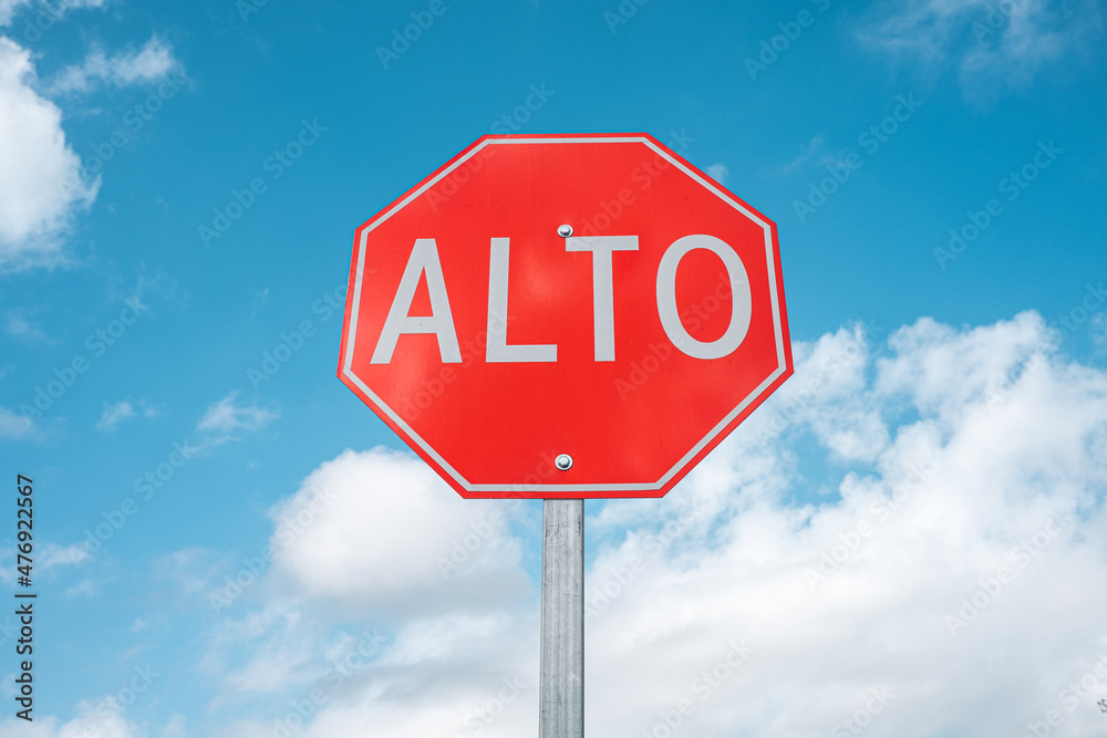 Red Stop sign in Spanish centered against the blue cloudy sky. Alto, background for text space. Red Stop sign in Spanish centered against the blue cloudy sky. Alto, background for text space.