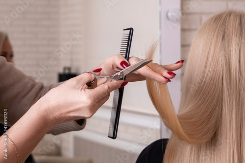 Hairdresser hands with brush and scissors cutting blonde hair in beauty salon