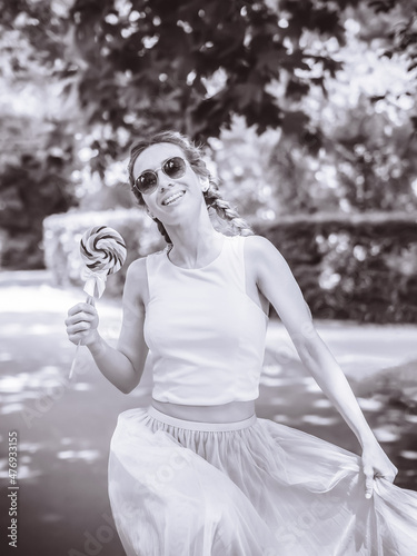Smiling lady with pigtails runs through the park holding a round lollipop with a spiral pattern. Black and white photo. Post-processing. Artistic effect