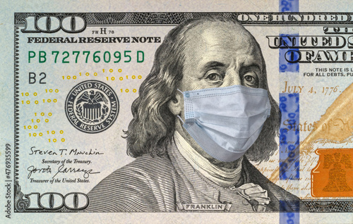 COVID-19 coronavirus in the USA and the world. Blue medical mask on Benjamin Franklin's face on a hundred-dollar bill. US dollar banknote during the world's coronavirus pandemic.