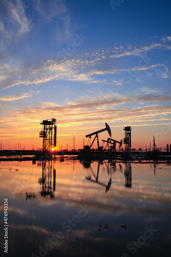 in the evening, oil pumps are running, The oil pump and the beautiful sunset reflected in the water, the silhouette of the beam pumping unit in the evening. © zhengzaishanchu