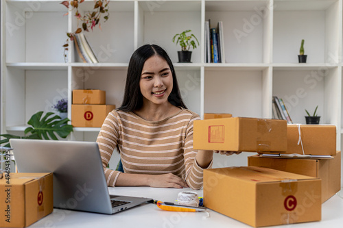 Asian woman checking parcel boxes for customers, she owns an online store, she takes orders from customers on the website and sends them through a private courier service. Online selling concept. © kamiphotos