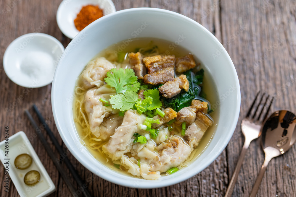 Egg Noodle in Clear Soup, Thailand Street Food, noodle with wonton and crispy pork serving with seasonings on wooden vintage table Egg Noodle in Clear Soup, Thailand Street Food, noodle with wonton and crispy pork serving with seasonings on wooden vintage table