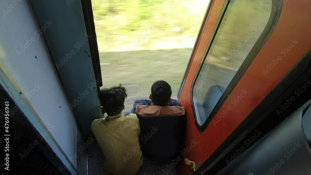Two young man sitting at the door edge of moving train, India Two young man sitting at the door edge of moving train, India