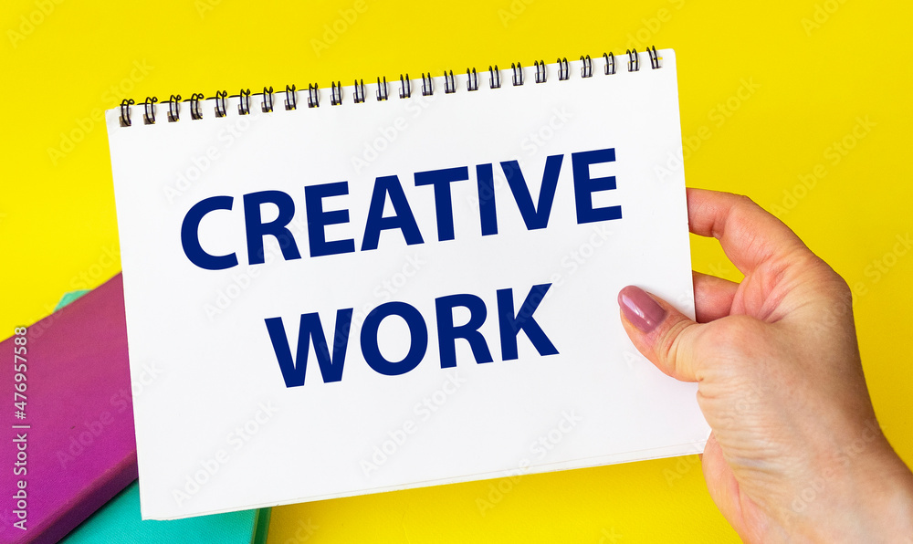 Creative work, the phrase is written on a notebook in the girl's hand on a yellow background. Creative work, the phrase is written on a notebook in the girl's hand on a yellow background.