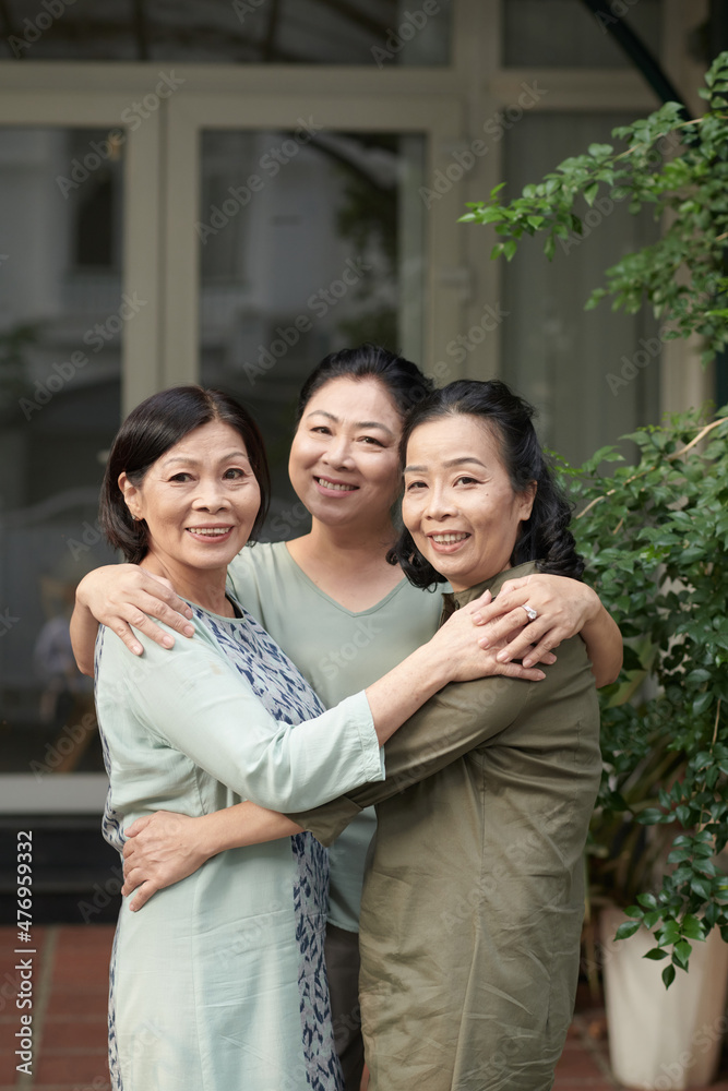 Portrait of hugging senior female friends standing at house front door Portrait of hugging senior female friends standing at house front door