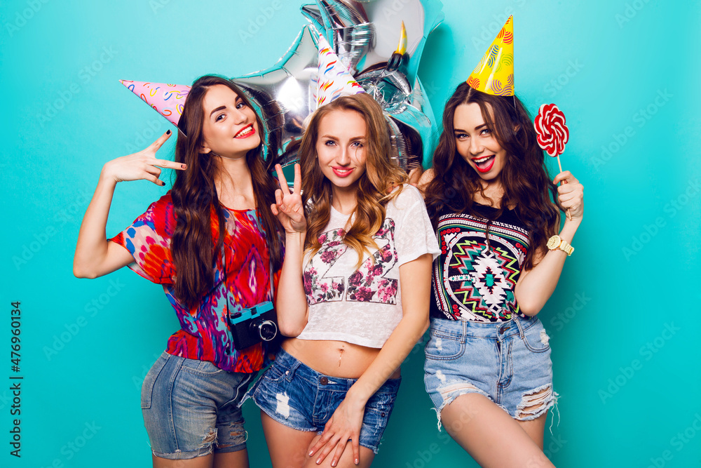 Three beautiful happy sexy woman in stylish summer outfit , paper hats and purity balloons having fun and celebrate birthday. Colorful blue background . Pretty girl hold big lollypop. Three beautiful happy sexy woman in stylish summer outfit , paper hats and purity balloons having fun and celebrate birthday. Colorful blue background . Pretty girl hold big lollypop.