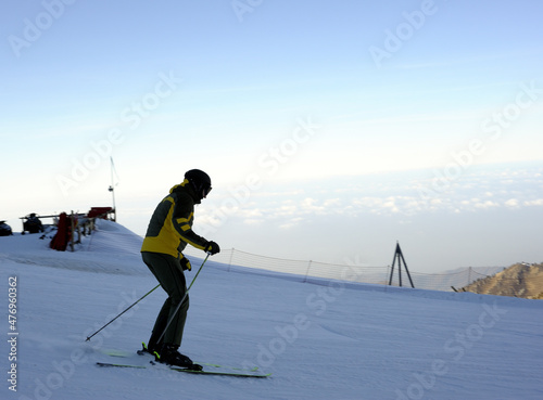 Active lifestyle and sports: rest in a ski resort. Skiing, snowboarding. Nice alpine view. Skiers and skateboarders are driving fast against the blue sky, above the clouds