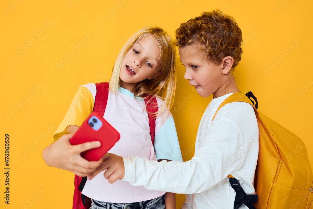 teenage boy and girl with school backpacks phone entertainment communication yellow background teenage boy and girl with school backpacks phone entertainment communication yellow background