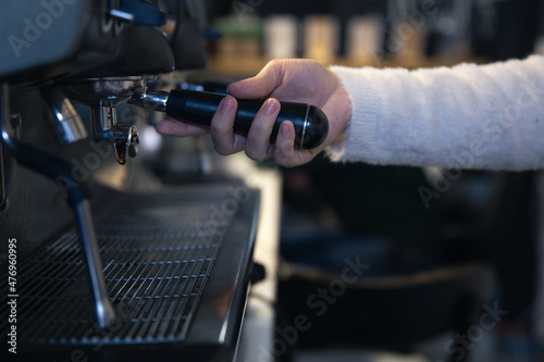 A female hand holds a holder in a professional coffee machine.