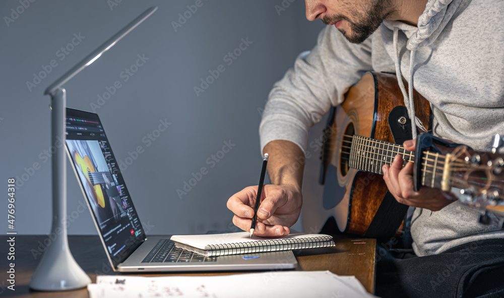 A man with a guitar in front of a laptop at a late hour learns to play. A man with a guitar in front of a laptop at a late hour learns to play.