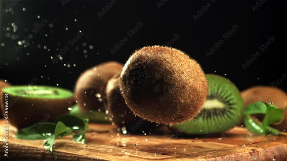 A ripe kiwi falls on a cutting board with splashes of water. On a black background. Filmed is slow motion 1000 frames per second.