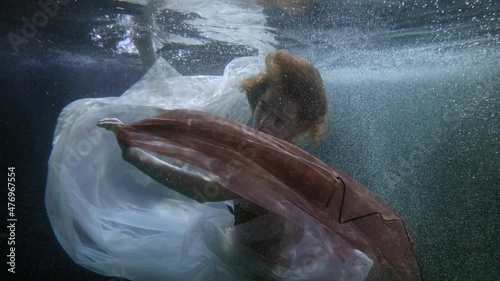beautiful young woman is floating alone underwater, portrait shot, slow motion, swaying hair