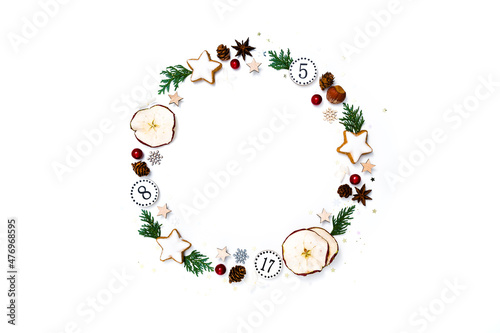 Christmas circle, Advent calendar arrangement. Wreath of fir tree branches, dried apple slices, pine cones, gingerbread cookies, anise, confetti stars, white background, flat lay, top view, copy space