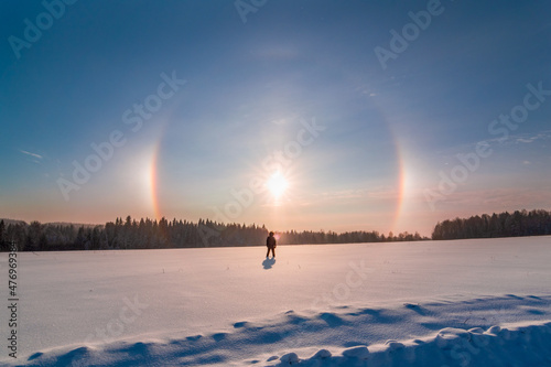 silhouette of a man standing in a snowy field and looking at the sun halo
