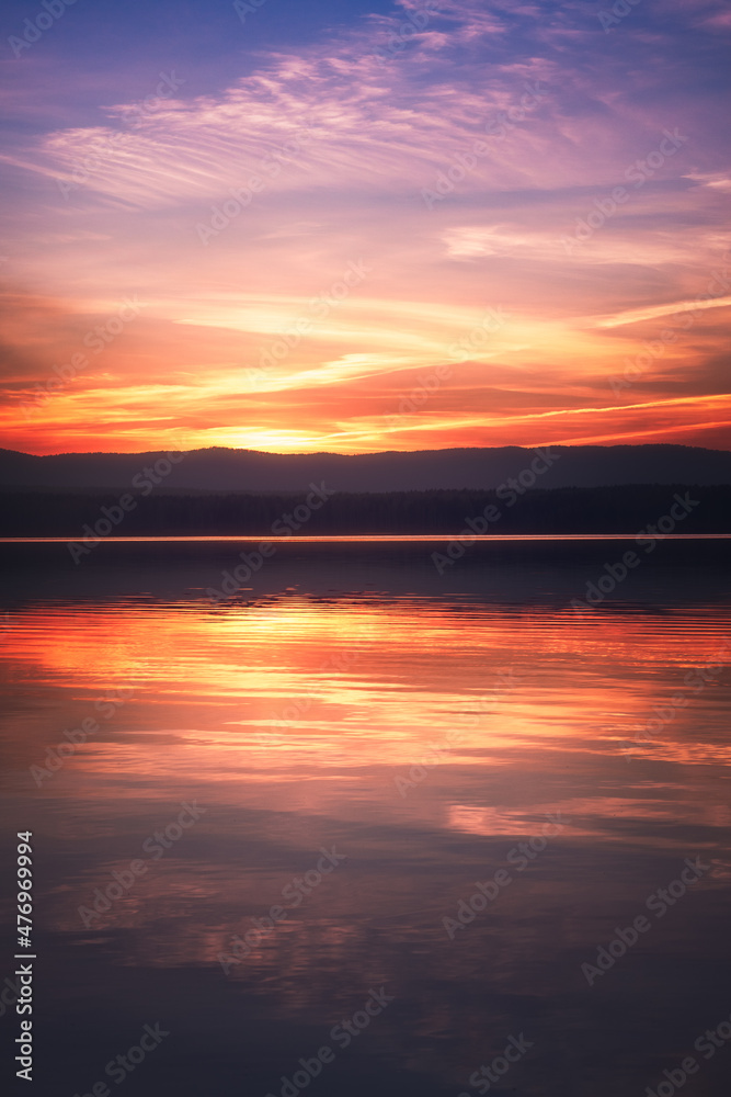 Beautiful colorful sunset sky and forest on the horizon reflecting in the water of the lake