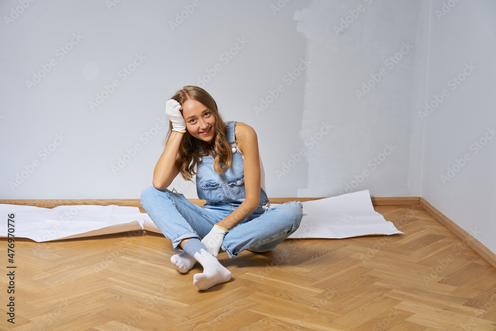 Young cute woman renovate and paint white color wall. Girl in blue denim overall happy to work Young cute woman renovate and paint white color wall. Girl in blue denim overall happy to work