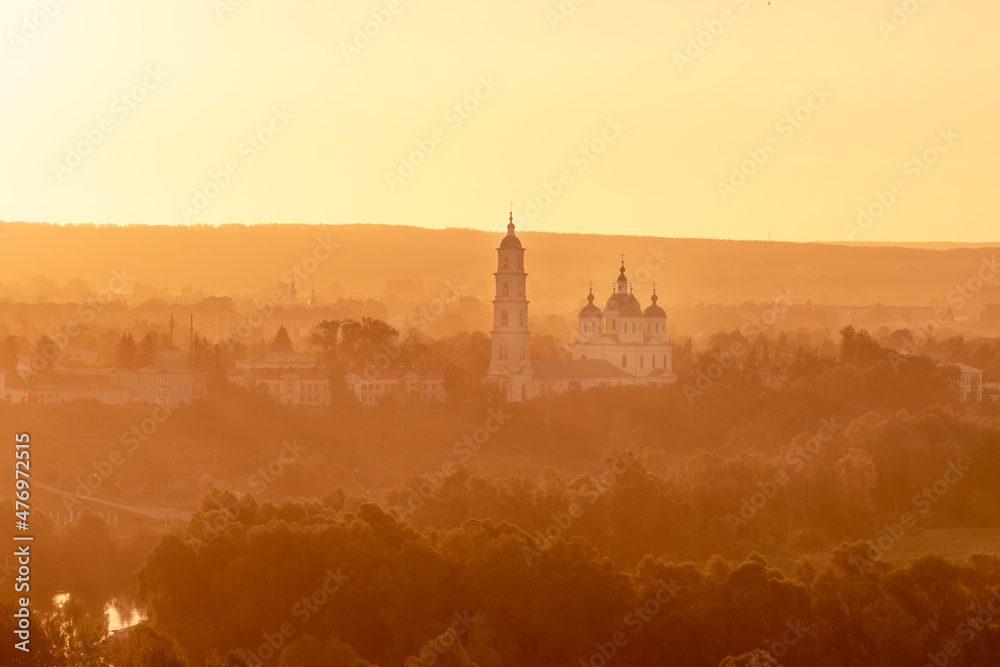 Naklejka premium Russian Orthodox Church in the morning fog at dawn in the middle of the forest lit by golden light