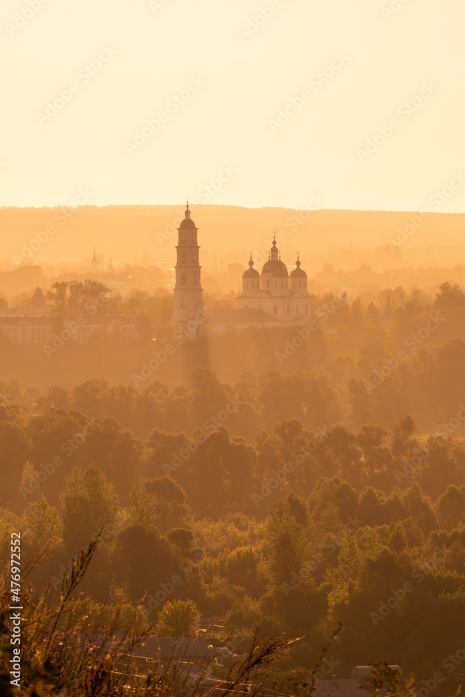 Russian Orthodox Church in the morning fog at dawn in the middle of the forest lit by golden light