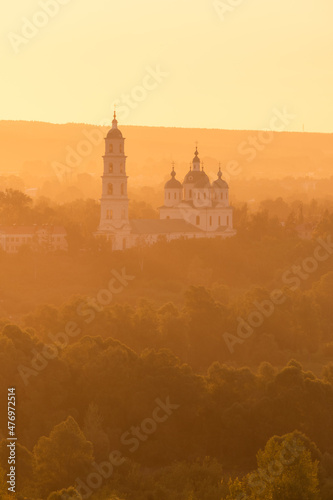 Russian Orthodox Church in the morning fog at dawn in the middle of the forest lit by golden light