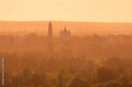 Russian Orthodox Church in the morning fog at dawn in the middle of the forest lit by golden light © Sergey Egorov