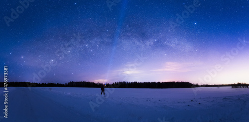 Milky Way Arc and sky full of stars above the snow field and a man with flashlight pointing in the sky