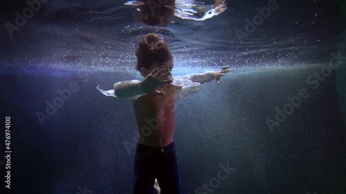 cute little boy is whirling inside water of swimming pool, child floating underwater