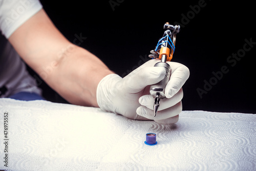 Obraz na plátně Hand of a tattooer, carefully holding a tattoo device.