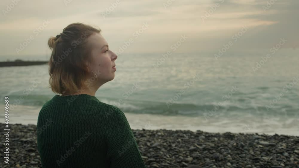 Girl sit looking sunset sea waves. Drinking coffee in green sweater. Rocky beach Girl sit looking sunset sea waves. Drinking coffee in green sweater. Rocky beach