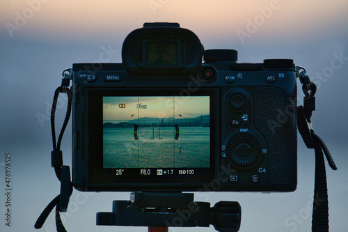 Photo camera on tripod taking picture of sunset in the sea, with unfocussed and bokeh background
