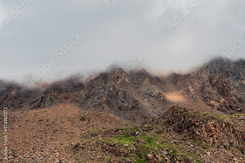 Natural background with high mountains, a steep mountain slope covered with rocks. The crest of the mountain under heavy low clouds.