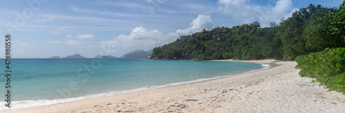 Large-format panoramic photo with high resolution of a typical Seychelles landscape. A perfect snow-white beach. In the distance, on the green hills, there are bungalows with thatched roofs. © Vadim