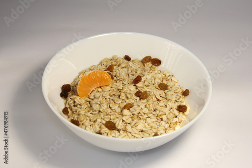 Oatmeal with tangerine slices and raisins. In a white bowl.