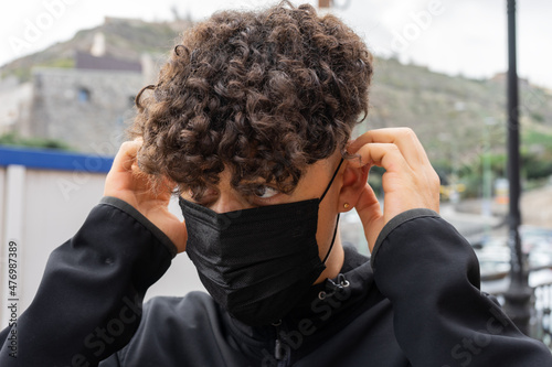 Un chico joven poniendose la mascarilla en la calle photo
