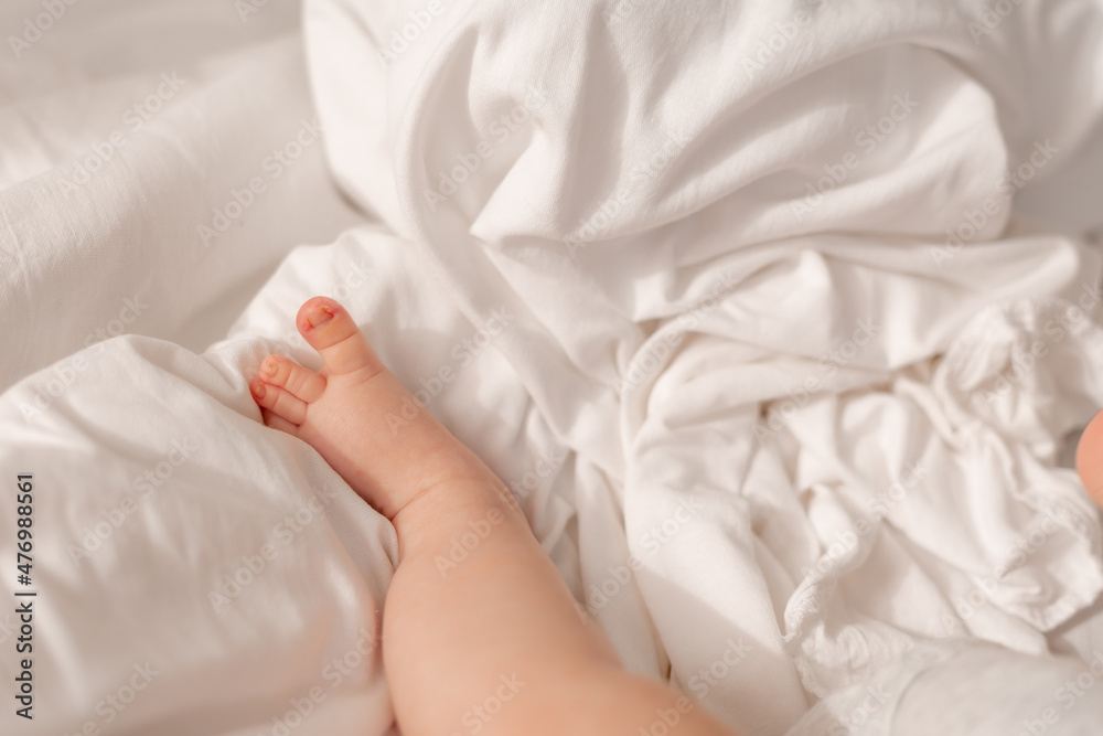 closeup of the bare feet of a baby in a white bodysuit lying on a white bed. High quality photo closeup of the bare feet of a baby in a white bodysuit lying on a white bed. High quality photo