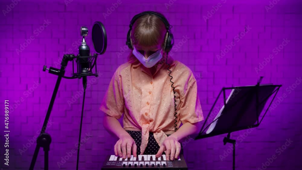 The end of the DJ girl's performance at the club during the pandemic. A female musician plays a drum midi keyboards, removes a protective mask, professional headphones, smiles looking into the camera