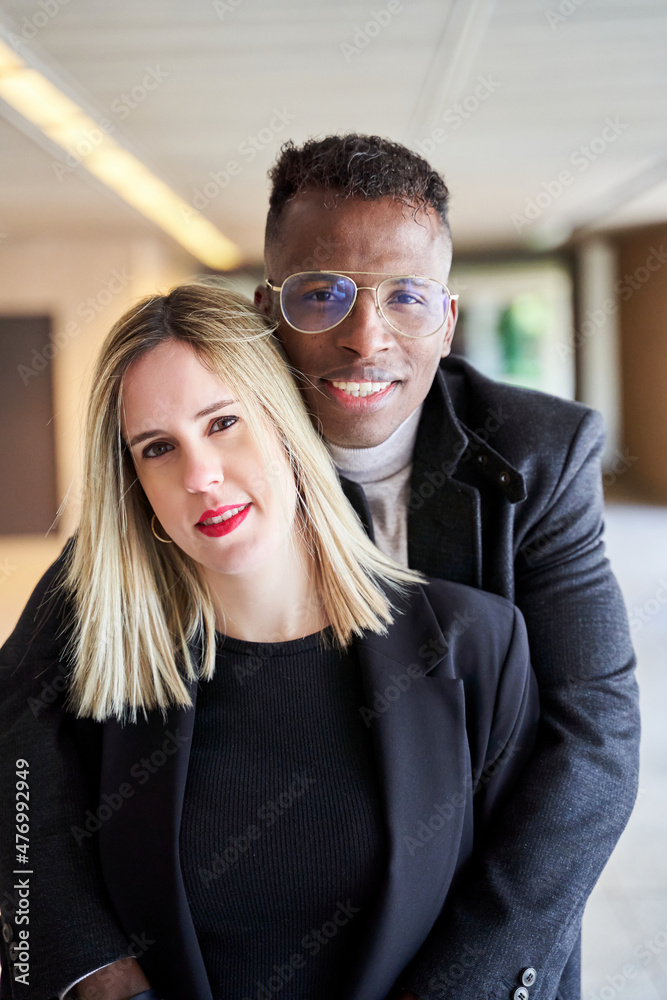 Glad African American man in glasses smiling and looking at camera while embracing blond woman during romantic date Glad African American man in glasses smiling and looking at camera while embracing blond woman during romantic date
