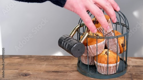 delicious biscuit cupcakes locked in an iron cage, rustic wooden table, hand reaches for sweets, concept of an outdoor tea party, unhealthy eating, calorie restriction, sweet life locked up photo