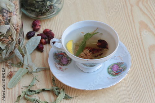 Herbal tea in the porcelain tea cup. Linden, rosehip(dog rose) and lemon balm(natural melissa) tea with lemon. Dried linden, rosehips and lemon balm on wooden floor and in jars. Healthy lifestyle.