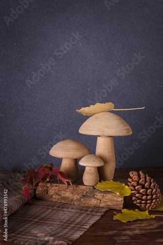 Wooden toy mushrooms, dry autumn leaves, pine cones on fabric napkin, deep grey background. Vertical shot, copy space. photo