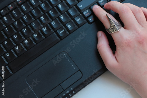 Businessman hand on the laptop. Hand writing on a keyboard of a laptop. Working at home office. Hand on keyboard. Embroidered silver ring on man's finger. Thumb Ring in Traditional. Silver man ring. photo