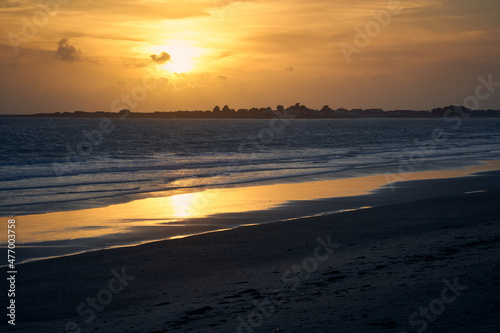 Sunset on the beach in France. City silhouette against blue sea water. Light of sun reflected in wet sand. France, Brittany, Gavres.