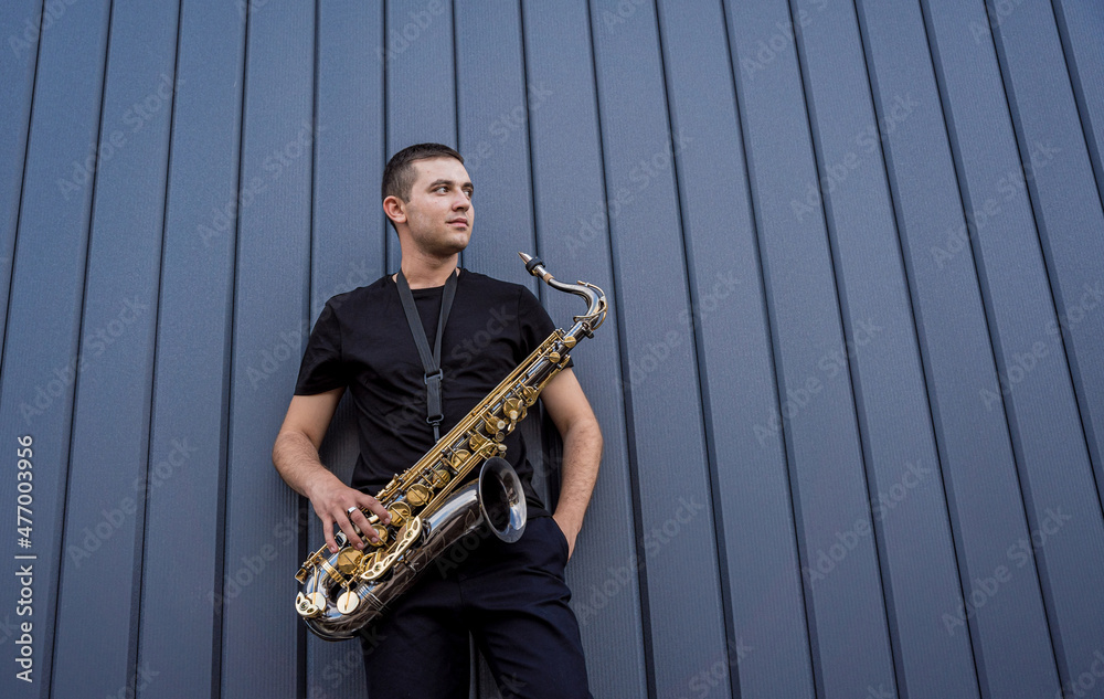 Fototapeta premium Young street musician playing saxophone near the big blue wall
