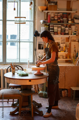 Young woman potter maker work with clay on pottery wheel in creative art space, professional studio. Female artist creating handicraft ceramics for hobby. Relax at handcraft products workshop concept