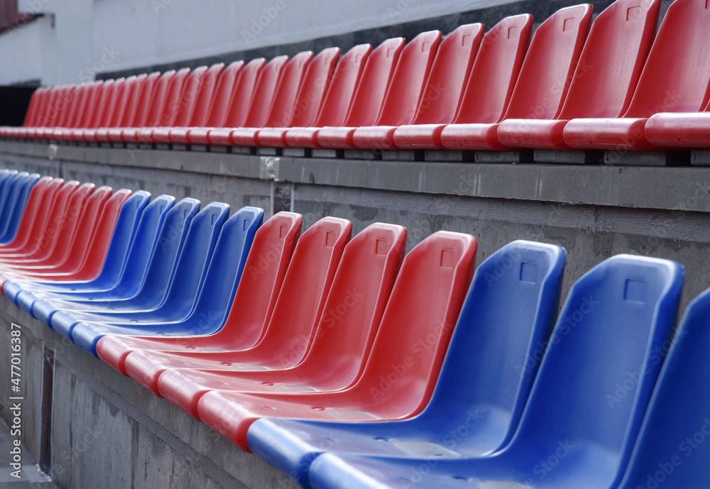 Fototapeta premium Plastic red and blue chairs are placed before the start of the match in an empty sports stadium.