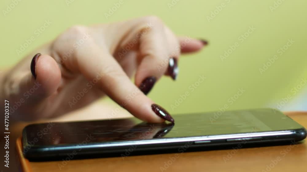 Close-up of a female hand clicks on the smartphone screen, views content. Female fingers with manicure are clicking on the screen of the gadget in search of interesting news. selective focus Close-up of a female hand clicks on the smartphone screen, views content. Female fingers with manicure are clicking on the screen of the gadget in search of interesting news. selective focus