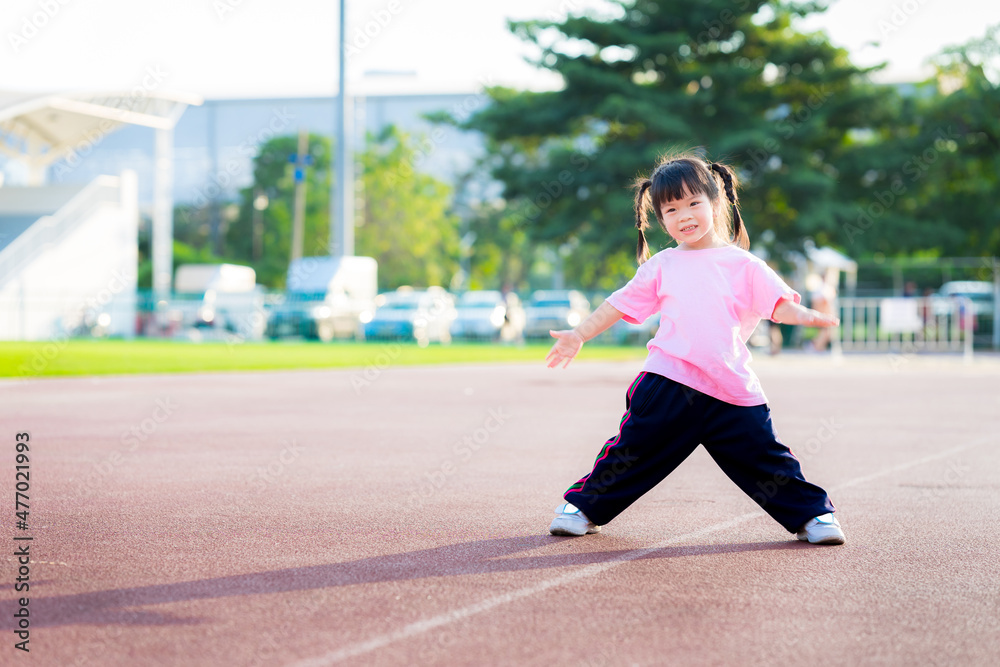 Child wearing pink t shirt is standing exercising. Kid smile and laugh, having fun making various gestures. Summer or spring evenings. Kindergarten children are 4 years old. Child wearing pink t shirt is standing exercising. Kid smile and laugh, having fun making various gestures. Summer or spring evenings. Kindergarten children are 4 years old.