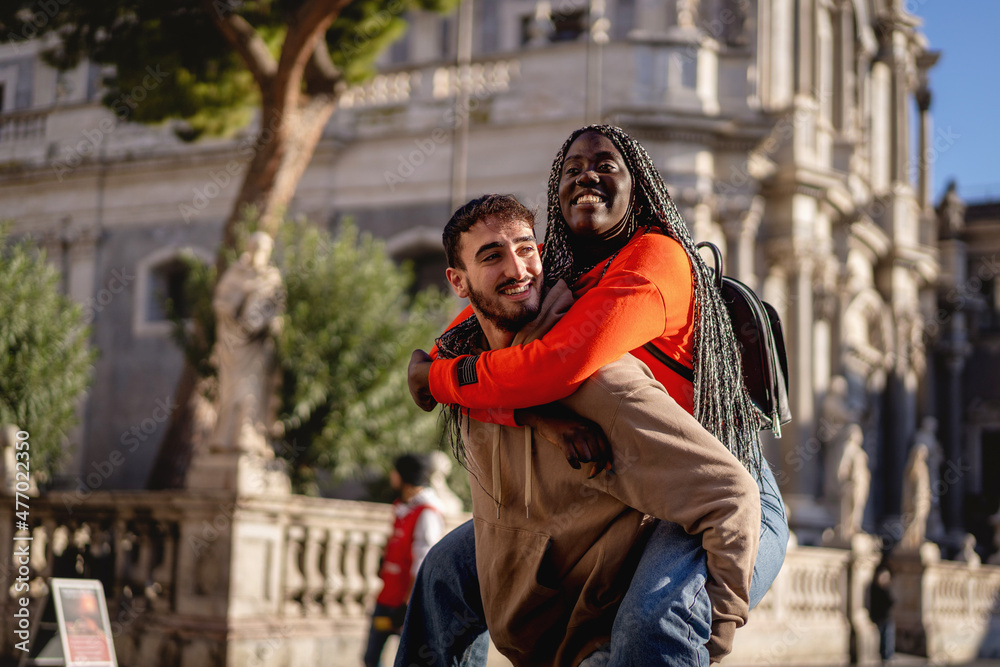 Multiracial couple of young lovers piggybacking in a baroque city center