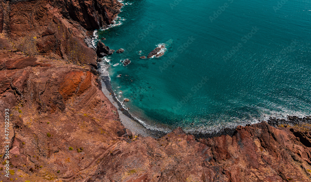 Atlantic ocean coastline with red rocky cliff, hiking path, turquoise waves and sea foam. Madeira island, Portugal. Aerial photography from drone. Breathtaking landscape.
